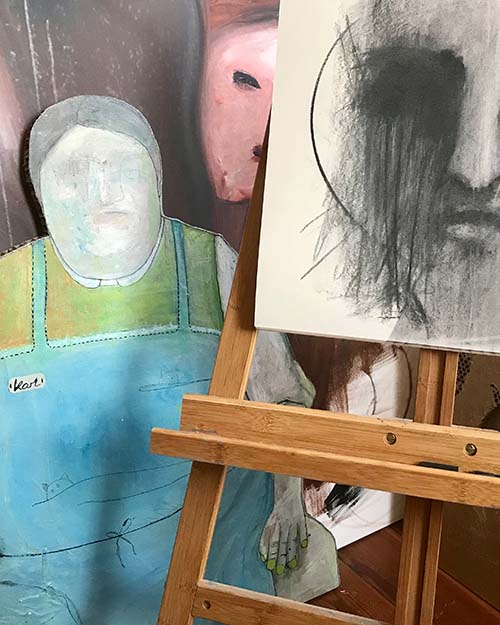 Photo of the artist's studio with two half-finished oil paintings and a portrait drawn with black charcoal.